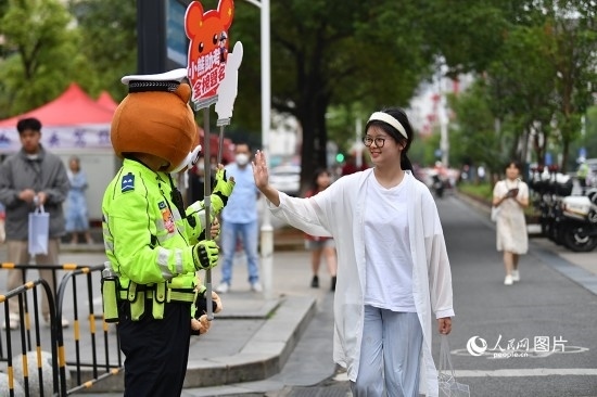 6月7日上午9時，隨著鈴聲的響起，2023年江西高考正式開考，江西省的53.57萬考生以縣（區(qū)）為單位隨機(jī)安排在全省256個考點(diǎn)、18968個考場參加高考。圖為“小熊交警”和考生擊掌鼓勵。 人民網(wǎng)記者 時雨攝