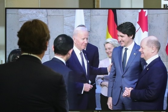 2022年3月24日，在比利時(shí)布魯塞爾的北約總部，一名男子觀看屏幕上美國(guó)總統(tǒng)拜登（右四）、歐盟委員會(huì)主席馮德萊恩（右三）、加拿大總理特魯多（右二）、德國(guó)總理朔爾茨（右一）出席七國(guó)集團(tuán)峰會(huì)合影儀式的畫(huà)面。新華社記者鄭煥松攝