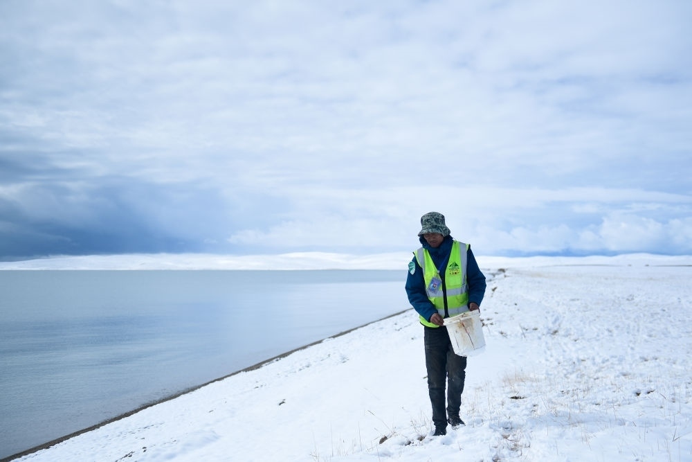 2021年10月20日，在青海省果洛藏族自治州瑪多縣扎陵湖鄉(xiāng)勒那村，三江源國家公園黃河源園區(qū)生態(tài)管護(hù)員在扎陵湖邊撿拾垃圾。新華社記者 張龍 攝
