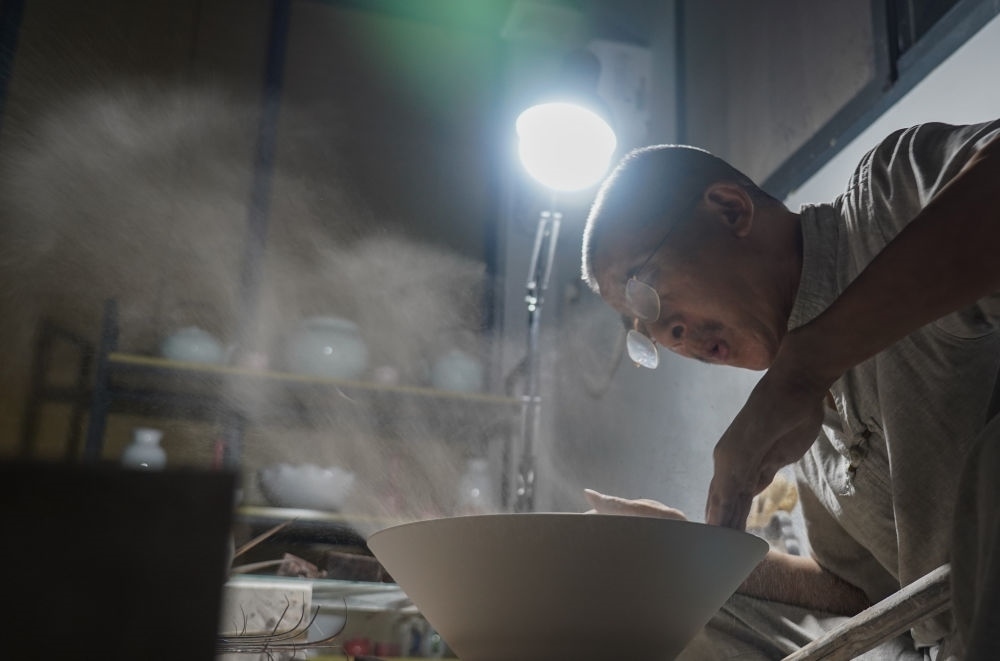 ↑ 在景德鎮(zhèn)，手工匠人吹去坯內(nèi)的泥土（2021年7月14日攝）。