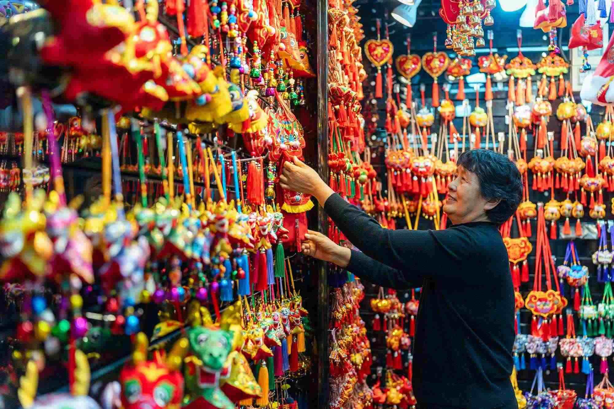 2023年12月11日，金華義烏國際商貿城，龍年喜慶用品掛滿攤位，顧客正在挑選中。