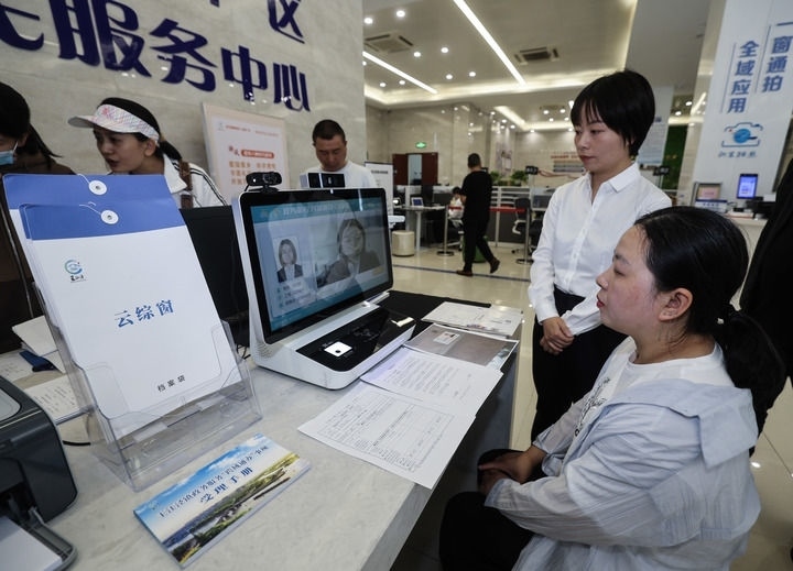 在浙江省嘉興市秀洲區(qū)王江涇鎮(zhèn)便民服務(wù)中心的“跨域通辦·云綜窗”窗口，辦理開(kāi)業(yè)登記的個(gè)體工商戶(hù)（右一）通過(guò)該系統(tǒng)與江蘇省蘇州市吳江區(qū)盛澤鎮(zhèn)行政審批局工作人員視頻連線，進(jìn)行身份讀取及材料線上審核（2024年5月9日攝）。新華社記者 徐昱 攝