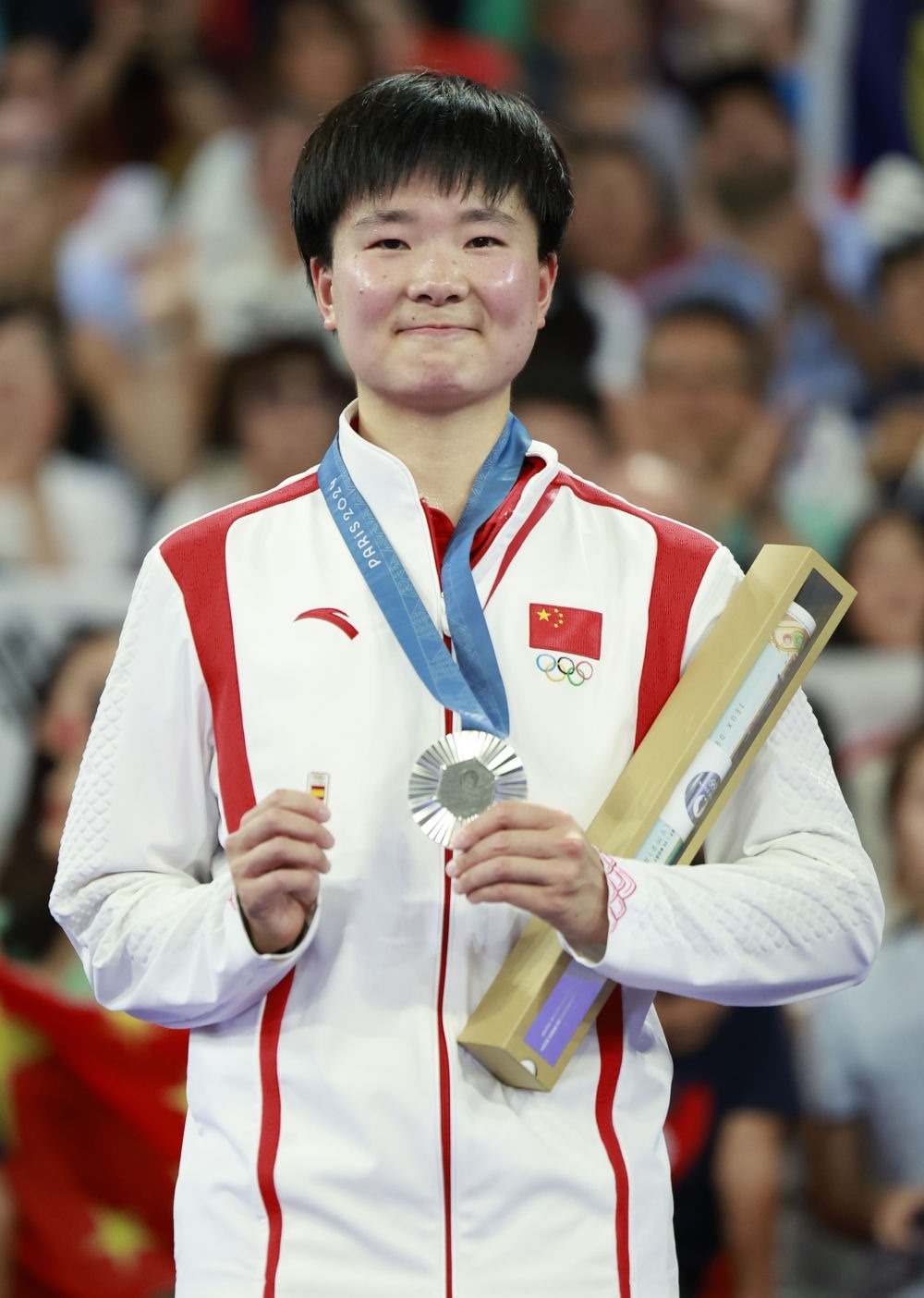 巴黎奧運(yùn)會羽毛球女子單打亞軍、中國選手何冰嬌在頒獎儀式上一手握著銀牌，一手握著西班牙奧委會徽章（2024年8月5日攝）。新華社記者 任正來 攝