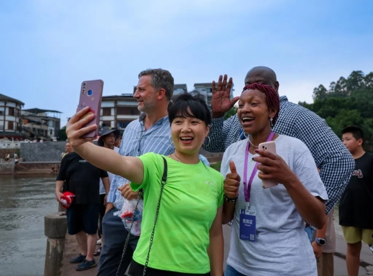 2024“一帶一路”媒體合作論壇聯(lián)合采訪調(diào)研行成員在樂山蘇稽古鎮(zhèn)與游客合影留念。本報記者 伊霄攝