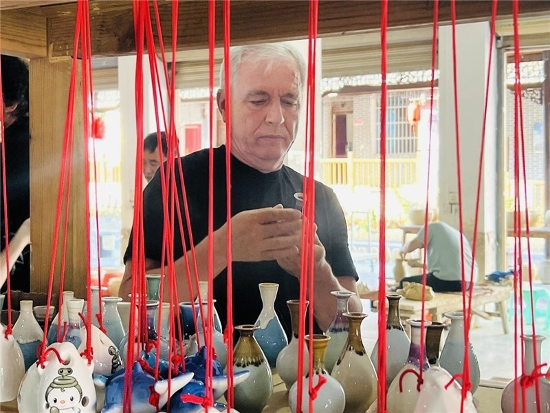 鄉(xiāng)愁如同一根根紅線，將游子與故鄉(xiāng)永遠(yuǎn)地牽連到一起?；逄账囄幕瘎?chuàng)意一條街的母氏陶藝館內(nèi)，紅線吊著陶瓶，思緒游走萬里。摩爾多瓦“信息標(biāo)簽”通訊社社長(zhǎng)亞歷山大·塔納斯端詳著館內(nèi)展示的陶藝作品，并挑選出心儀的小擺件帶回摩爾多瓦，也帶走花茂村的“鄉(xiāng)愁”。（張亞欣攝）