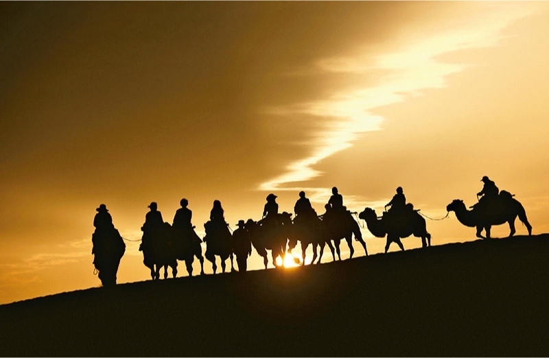 新時(shí)代以來，文化和旅游深度融合發(fā)展體制機(jī)制不斷健全，成功走出了一條獨(dú)具特色的中國旅游發(fā)展之路。圖為2024年9月1日清晨，游客在甘肅省敦煌市鳴沙山月牙泉景區(qū)乘騎駱駝，欣賞大漠風(fēng)光，體驗(yàn)絲路風(fēng)情。 新華社發(fā) 張曉亮/攝