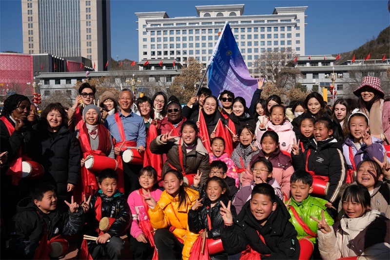 中外青年學(xué)子在安塞文化廣場觀看陜北腰鼓和大秧歌表演后合影留念，大家踏著鼓點共舞，翻飛的紅綢與躍動的身影交織，在黃土地廣場上繪出一幅生動的陜北民俗互動畫卷